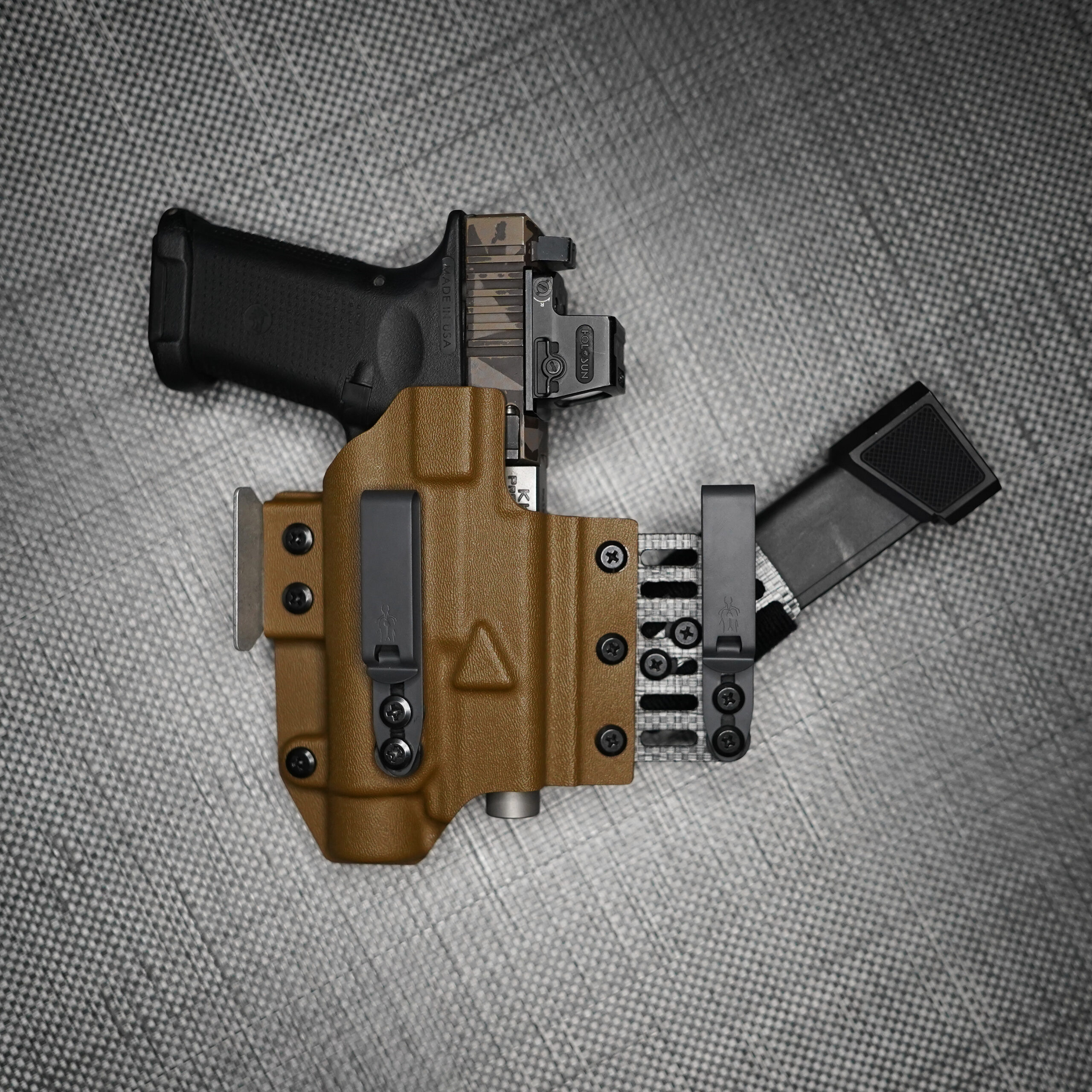 Glock pistol with TLR-1 HL weapon light in a coyote brown holster with sidecar magazine carrier, laid on a gray textured background